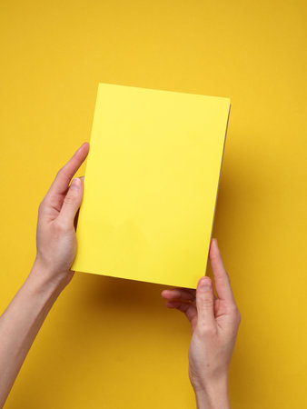 Hands holding a notebook with a yellow cover on yellow backgroundの写真素材