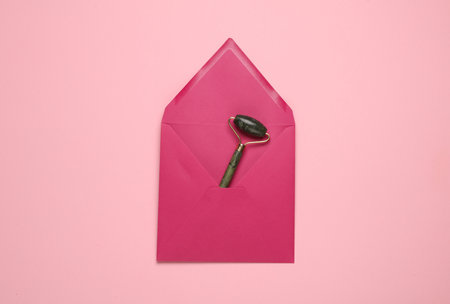 Envelope with a jade massage roller on pink background. Beauty conceptの写真素材