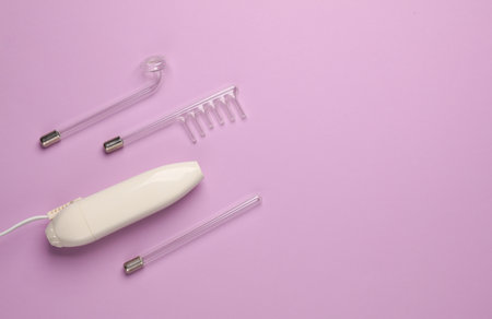 Acne treatment. Device for local darsonvalization with nozzles on a purple background. Beauty...