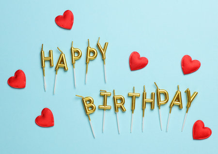 Golden candles letters in shape of happy birthday word with hearts on blue backgroundの写真素材