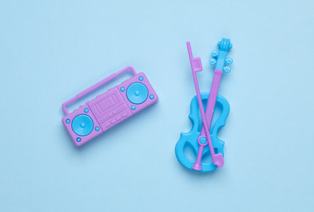 Miniature boombox audio tape recorder and violin on blue pastel background