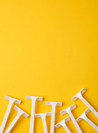 Disposable white plastic razors on yellow background with copy space. Top viewの写真素材