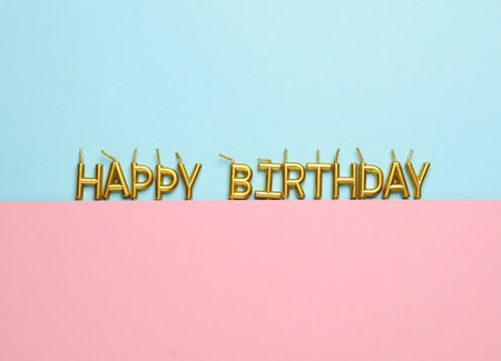 Golden candles letters in shape of happy birthday word on pink blue pastel backgroundの写真素材
