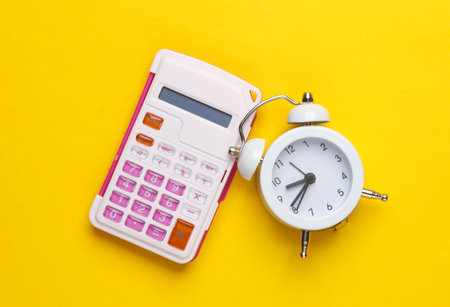 Calculator with alarm clock on yellow background. Time is moneyの写真素材
