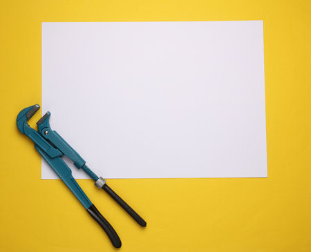 Metal adjustable wrench with blank paper sheet on yellow background.の写真素材
