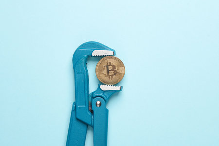 Metal adjustable wrench holding bitcoin on blue background. Business concept