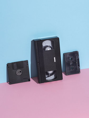 Floppy disk, video and audio cassette on pink blue pastel background. Retro 80s. Outdated technology. Creative layout, minimalism, trendy minimal still lifeの写真素材