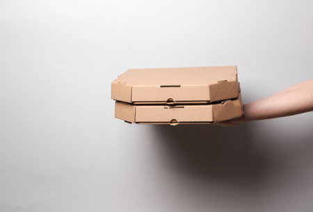 Hands holding craft pizza boxes on gray background with shadowの写真素材