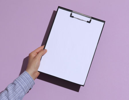 Man's hand in shirt holding blank clipboard on purple pastel background with shadowの写真素材