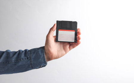 Man's hand in denim shirt holding floppy disk on gray backgroundの写真素材