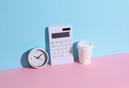 White calculator with clock and coffee cup on blue-pink background with shadow. Business and finance concept. Creative mockupの写真素材