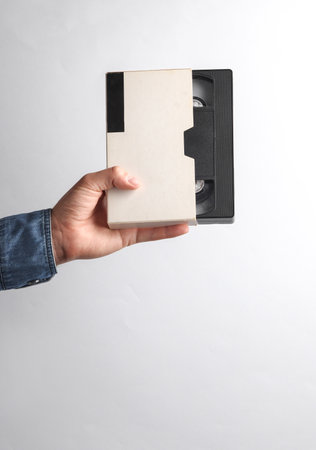 Man's hand in denim shirt holding vhs video cassette in box on gray backgroundの写真素材