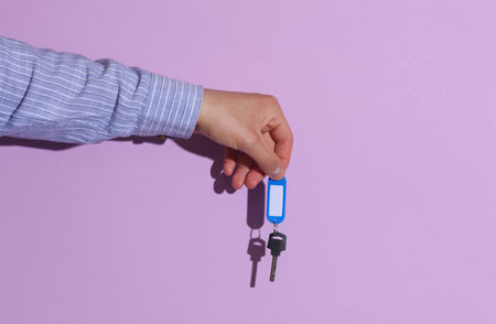 Man's hand in shirt holding keys with tag on purple pastel background