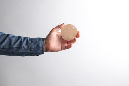 Man's hand in denim shirt holding craft round price tag on gray background. Sale conceptの写真素材