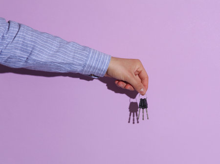 Man's hand in shirt holding keys on purple pastel background with shadowの写真素材