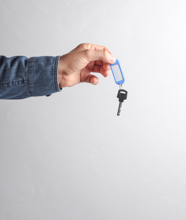 Man's hand in denim shirt holding key tag on gray backgroundの写真素材