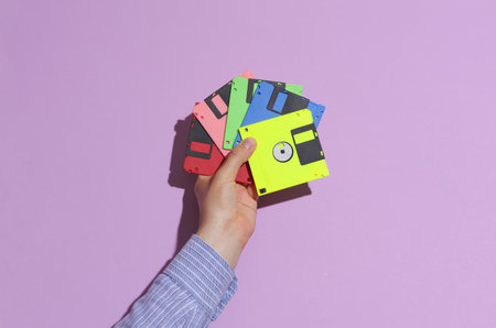 Man's hand in shirt holding colored floppy disks on purple pastel background with shadowの写真素材