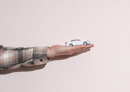 Man's hand in shirt holding toy car on beige background with shadowの写真素材