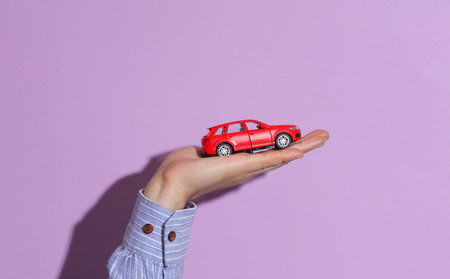 Man's hand in shirt holding red toy car on purple pastel background with shadow.の写真素材