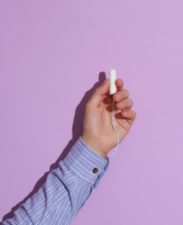 Man's hand in shirt holding tampon on purple pastel background with shadow.の写真素材