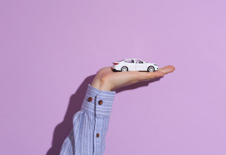 Man's hand in shirt holding toy car on purple pastel background with shadow.の写真素材