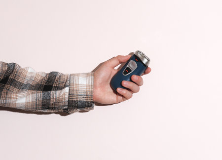 Man's hand in shirt holding electric shaver on beige pastel background with shadow