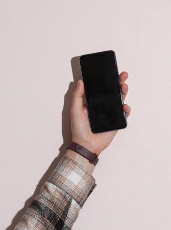 Man's hand in shirt holding smartphone on beige background with shadowの写真素材