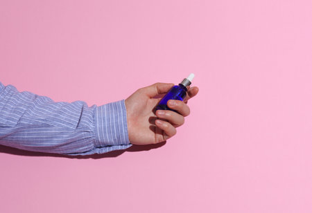 Man's hand in a shirt holding serum bottle on pink background