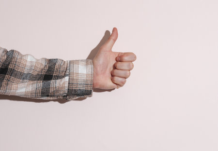 Man's hand in shirt shows a thumbs up on beige backgroundの写真素材
