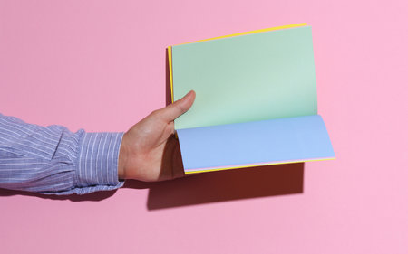 Man's hand in shirt holding open notebook on pink background with shadowの写真素材
