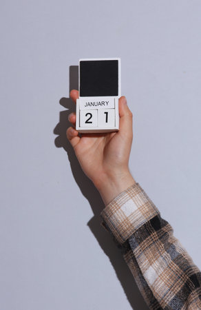 Man's hand in shirt wooden holds block calendar organizer with date January 21 on gray background with shadowの写真素材