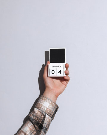 Man's hand in shirt wooden holds block calendar organizer with date January 4 on gray background...