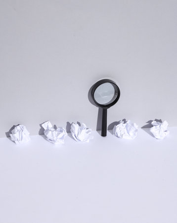 Magnifying glass with crumpled paper balls on white background with shadow. Search for creative ideas, business conceptの写真素材