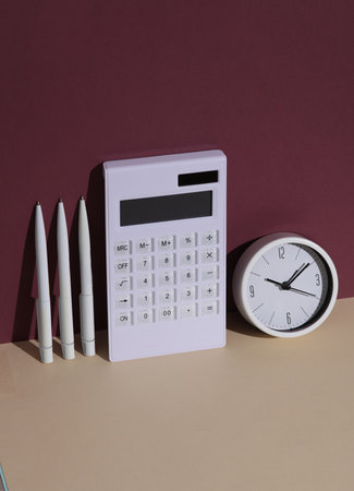 Creative business layout. Calculator with clock, pens on burgundy beige background with shadowの写真素材