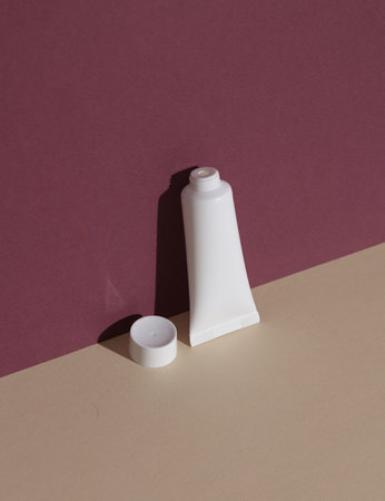 White cream tube on burgundy beige background with shadow. Creative beauty layout. Mockup, template for designの写真素材