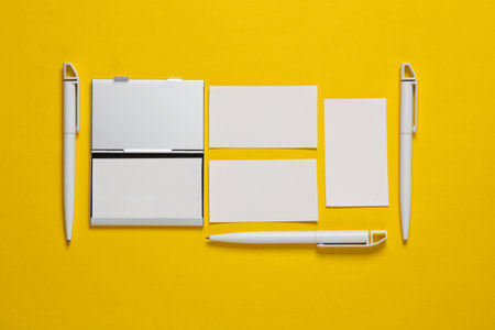 Metal box business card holder with business cards and pens on a yellow backgroundの写真素材