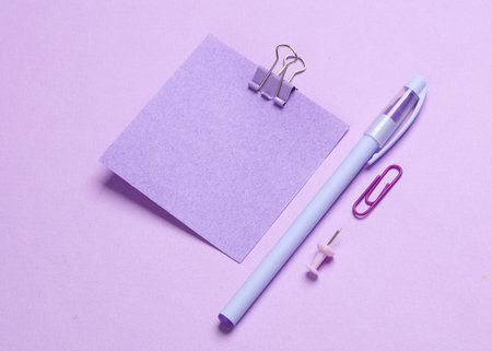 Blue stationery accessories on purple pastel background. Memo papers, pen, paper clips, pins....