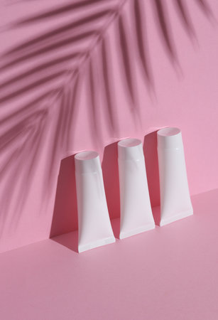 White cream tube on pink background with palm leaf shadow. Creative beauty layout. Mockup, template for designの写真素材