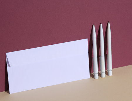 White pens with envelope on burgundy beige background. Minimalism, conceptual business photo, creative layoutの写真素材