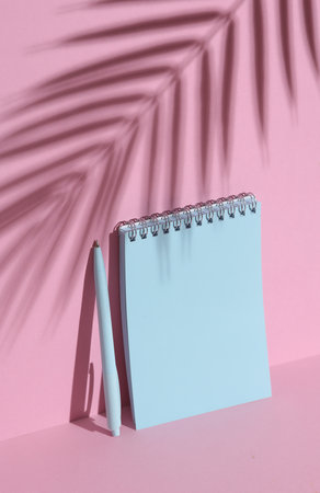 Blue notebook and pen on a pink background with palm leaf shadow. Creative layout, minimalismの写真素材
