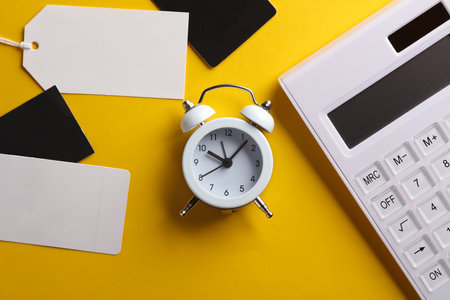 Calculator with alarm clock and price tags on yellow background. Sale, shopping concept