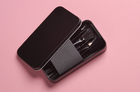 Set of black make-up brushes in metal box on pink background. Beauty concept