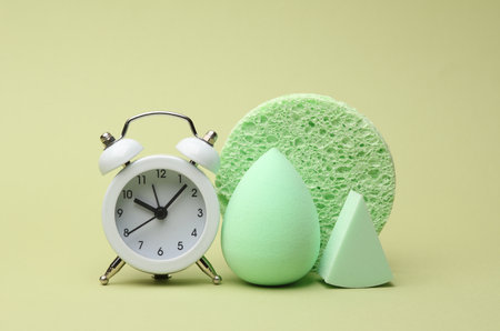 Alarm clock, Remover sponge and make-up blenders on green background. Beauty concept
