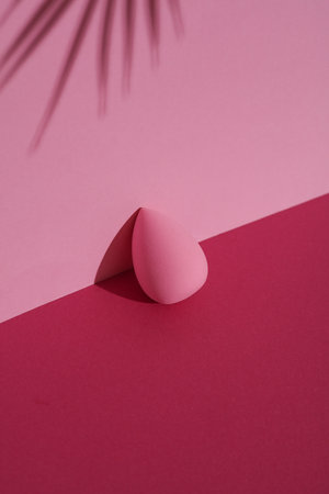 Makeup sponge blender on a pink background with palm leaf shadow. Beauty concept. Creative layout, minimalismの写真素材