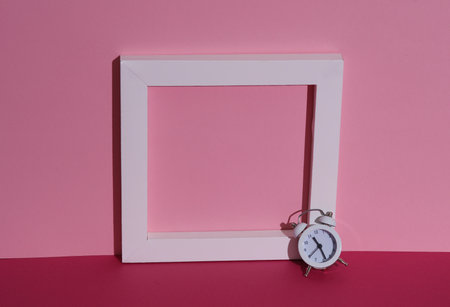 White frame with alarm clock on pink background with shadow. Creative layout, minimalismの写真素材