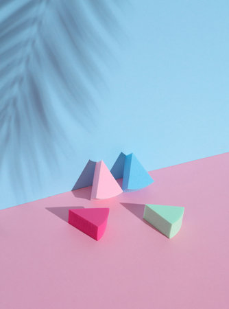 Makeup sponges blenders on a pink blue background with palm leaf shadow. Beauty concept. Creative...