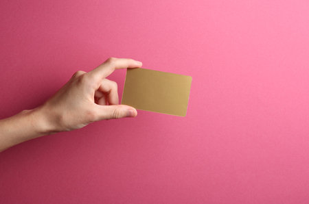 Golden business card in a female hand on a pink backgroundの写真素材