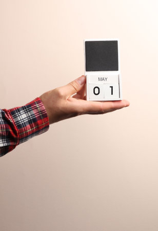 Date May 1, block calendar in male hand on beige background