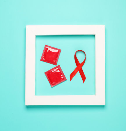 Red AIDS awareness ribbon and condoms in a white square frame on blue background. Minimal medicine...