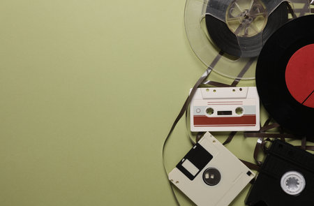 Floppy disk, vinyl record, film reel, vhs and audio cassette on green background. Retro 80s. Copy...